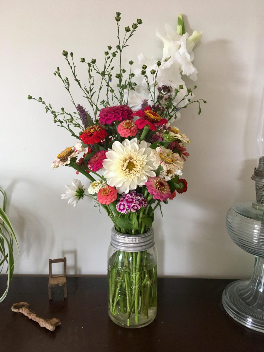 Vase of seasonal flowers including dahlia and zinnia, old rusted skeleton key, small handmade wooden dollhouse chair